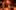 17-BarberShop-lightbulb-Marc-Brenner-2000x1000-1-aspect-ratio-16-10 On a warmly lit stage, a man sits in an office chair smiling and touching his head, in front of him there are various barber shop accessories on a cabinet, and another man standing contorting his face.