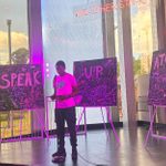 A person stands on a stage in front of three chalkboards with words 