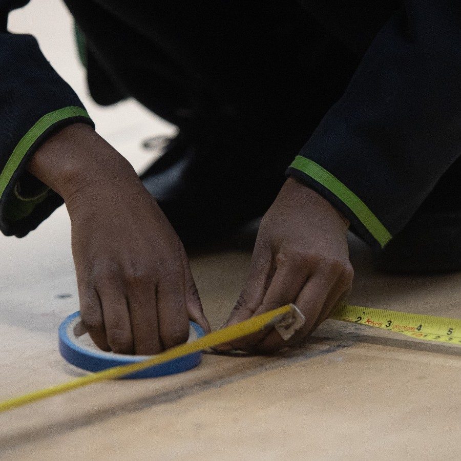 22-YoungTechs-forSM-markings-2000x1000 A pair of hands marking up a floor with measuring tape.