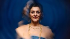 A-Tupperware-of-Ashes-National-Theatre-245x138 A blurred or shaken photo of a woman (Meera Syal), smiling and wearing gold jewellry and a blue dress.