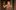 AANT-DRESS-CIRCLE -NTL-2019-One-Man-Two-Guvnors-2011-PRO-7-James-Corden-as-Francis-Henshall-Johan-Persson-2000x1250 A person (James Corden) in a plaid suit holds up a single red rose. They are standing indoors, with a neutral expression, and the background is a blurred wooden interior.