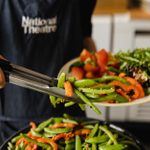 Runner beans and carrots in sesame seeds being added to a plate of salad in the Atrium Cafe.