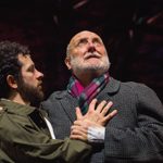 Two men with their arms around each other. One is wearing a green jacket and one is wearing a grey jacket.