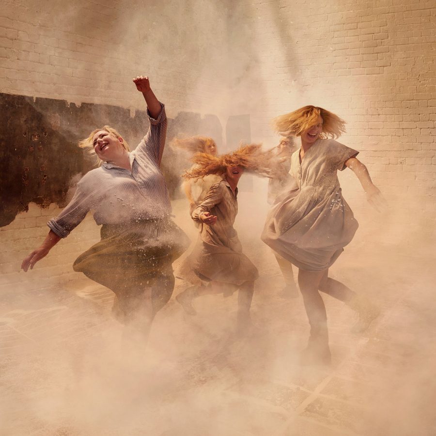 Dancing-at-Lughnasa-National-Theatre-2000x1000 A group of women dancing exuberantly, kicking up dust around them, smiling, wearing light cotton dresses and skirts