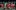 A group of men are in a group, they all wear red England kit and are in various stages of celebration after a goal. Some are on their knees, all are exclaiming. One of the men is in a green goalie uniform.