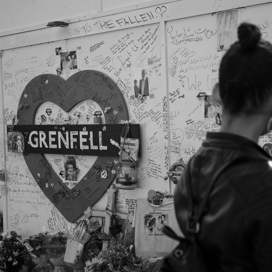 Grenfell-2000x1000-masthead-gold-and-ashes-photo-Feruza-Afewerki A mural of a heart-shaped tube sign with the words 'Grenfell' has been covered with messages for the bereaved. A woman stands silhouetted in the foreground, slightly out of focus.
