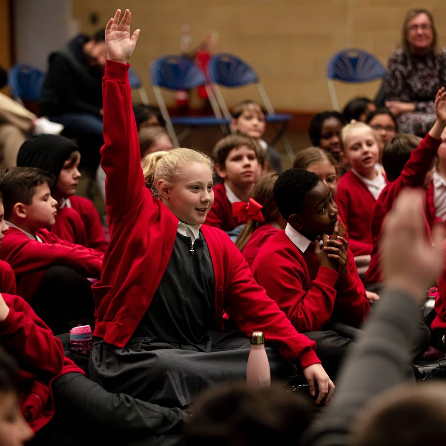 2023-Hamlet-School-HarryElletson-handintheair-2000-1000 A group of primary school children, in the centre a young person with their hand in the air