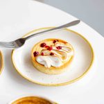 Lemon tart sitting on the edge of a white table with a fork resting on the white plate