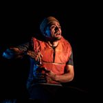 A man in an orange lifejacket, looking shocked and in the midst of pulling an object from his jacket
