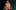 Nye-Take-Your-Seats-National-Theatre-1920x1080 A person (Michael Sheen) wearing striped pajamas stands against a bold, dark green and black gradient background, looking upward with a thoughtful expression.