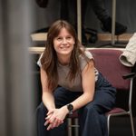Rebecca Frecknall sits in a chair while smiling and clasping her hands together.