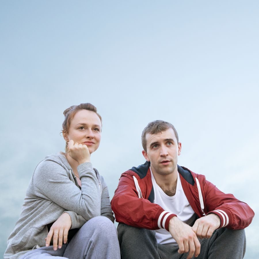 Romeo-and-Julie-poster-2000x1250 Romeo and Julie poster photo of Callum Scott Howells and Rosie Sheehy, wearing tracksuit tops and bottoms, sat side-by side against a hazy, blue sky