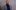 sir-damon-buffini-2000x1250-photo A person with a bald head and a beard, wearing a grey plaid blazer over a dark blue turtleneck, stands in front of a neutral, textured wall. They are smiling gently and looking directly at the camera.