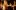 Women-of-Troy-2007-PRO-21-Stephen-Cummiskey-aspect-ratio-16-10 Six women stand in a dimly lit room with their arms raised to shoulder height, positioned as if ready to dance. They appear focused, each wearing semi-formal to formal attire. The background is industrial with exposed columns and pipes.