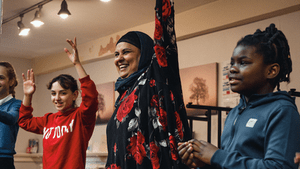 2022-DCC-redblacktop-Credit-Rasha-Kotaiche A woman in a headscarf with two young people either side of her with their hands in the air