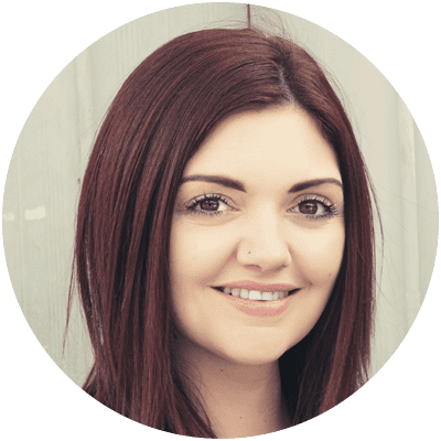 NIcole-Behan-circular-headshots-400x400 A person (Nicole Behan) with long, straight, dark hair is smiling softly. The background is blurred and light-colored. She is centered in a circular crop of the image.